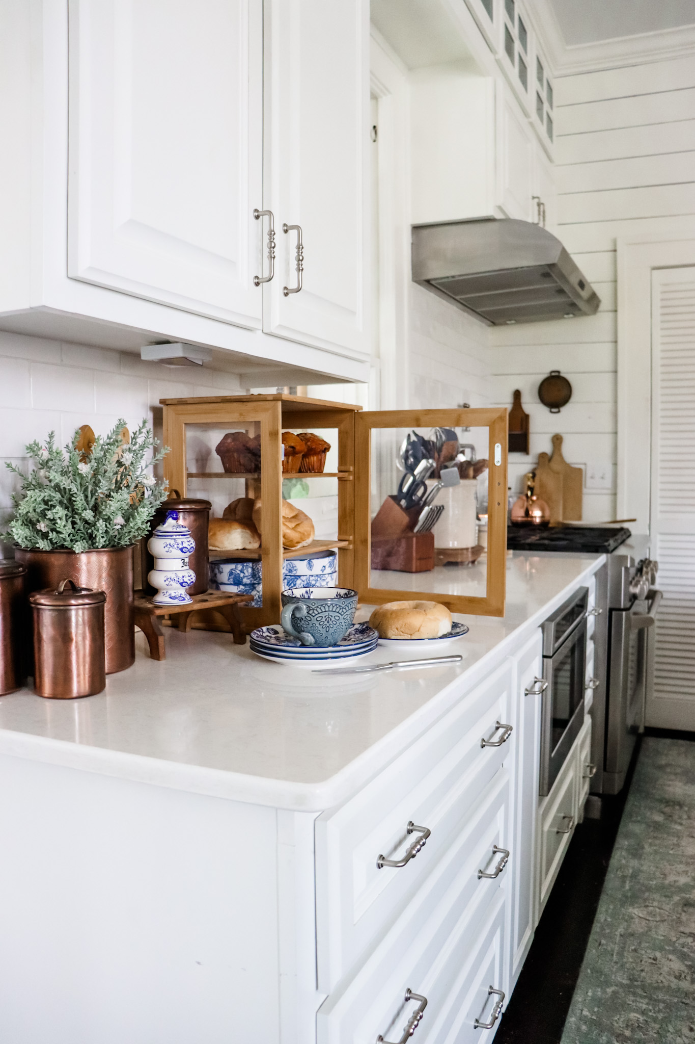 Copper canisters and a wood bread box pop against a cool white kitchen.